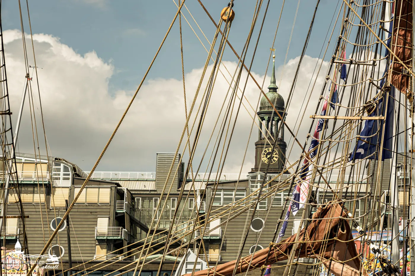 Blick auf den Hamburger Michel durch die Takelage eines historischen Segelschiffs im Hafen.