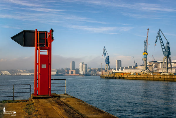 Hamburger Hafen mit roten Richtfeuer, Kränen und Stadtansicht im Hintergrund bei klarem Himmel.