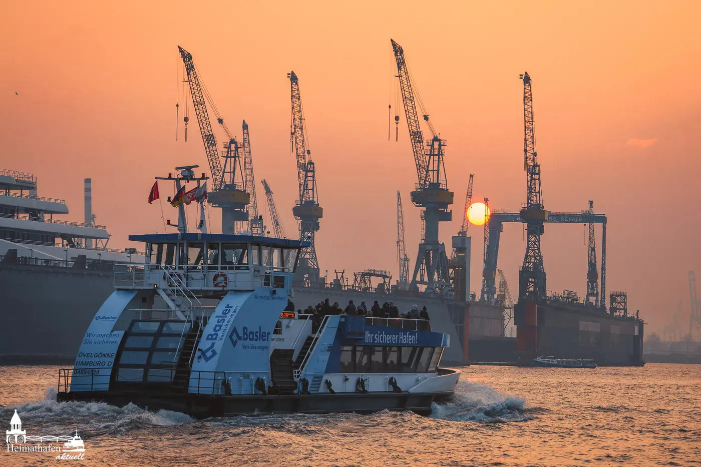 Hafenfähre bei Sonnenuntergang im Hamburger Hafen mit Werftkränen im Hintergrund