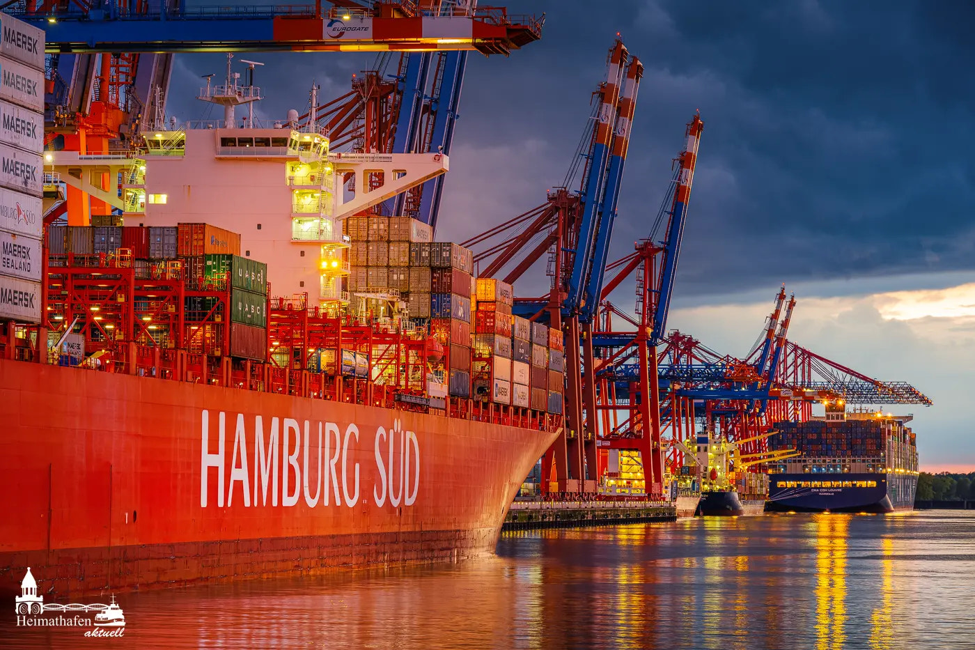 Das Containerschiff HAMBURG SÜD liegt am Waltershofer Hafen vor dramatischer Abendkulisse. Im Hintergrund ragen riesige Containerbrücken in den Himmel und weitere Containerriesen warten auf Abfertigung.