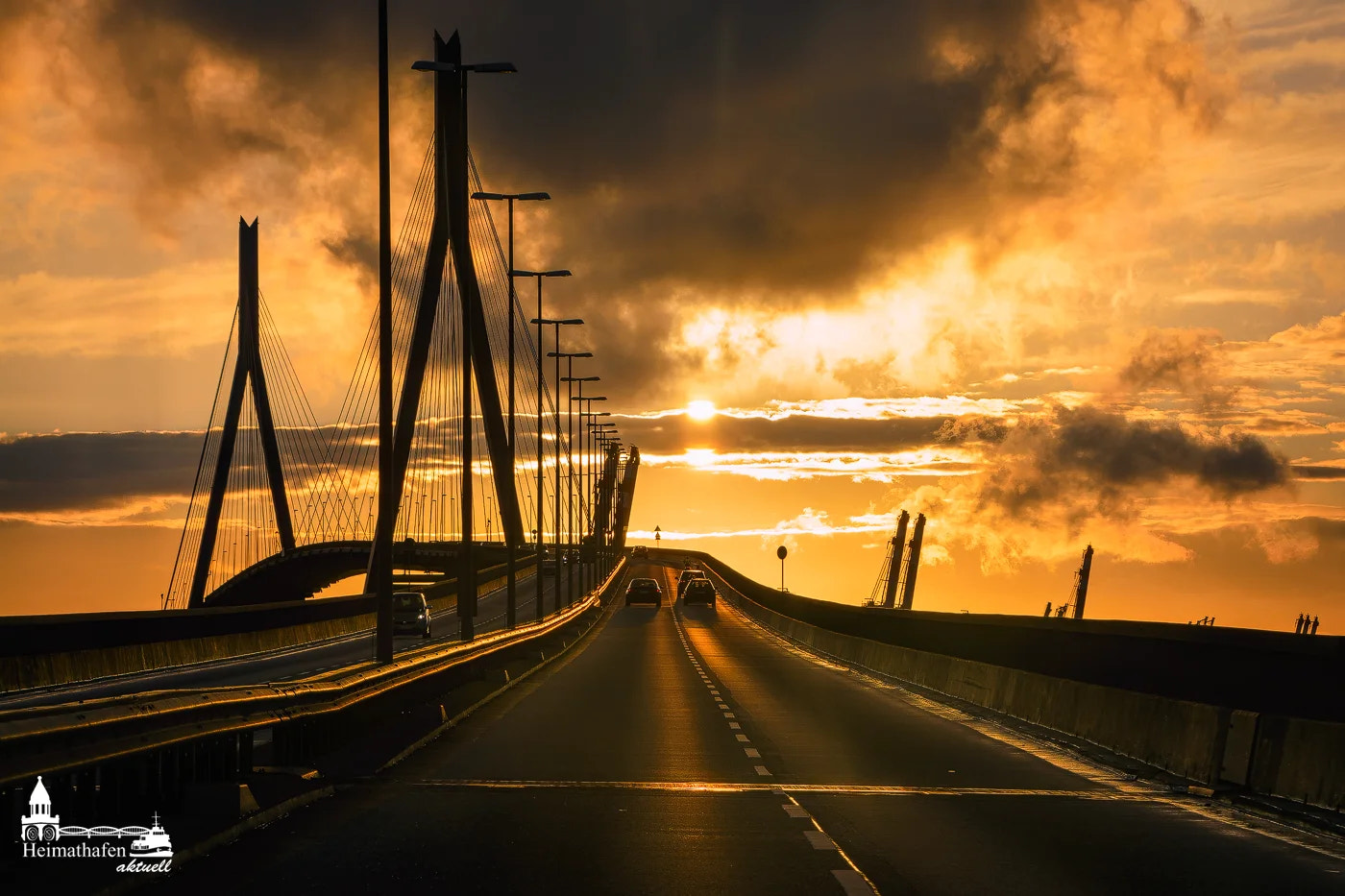 Köhlbrandbrücke bei Sonnenuntergang mit Autos auf der Fahrbahn und dramatischem Himmel im Hamburger Hafen