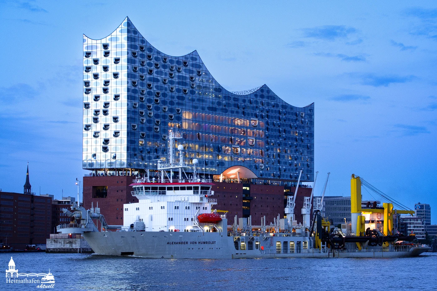 Schlickbagger ALEXANDER VON HUMBOLDT vor der Elbphilharmonie bei Abendlicht.