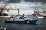 Polizeiboot „Bürgermeister Weichmann“ auf Streife im Hamburger Hafen mit Containerschiff und Kränen im Hintergrund.