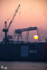 Die aufgehende Wintersonne leuchtet hinter den Hafenkränen von Blohm+Voss am Dock 11 – eine stimmungsvolle Szene voller Industriepracht und Morgentau.