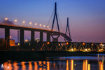 Die Köhlbrandbrücke erstrahlt bei Nacht – mit Lichtreflexionen im Wasser und leuchtenden Laternen entlang der eleganten Brückenkonstruktion.