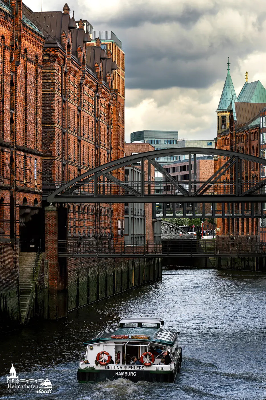 Barkasse BETTINA EHLERS fährt durch die historischen Fleete der Hamburger Speicherstadt unter dramatischem Himmel.